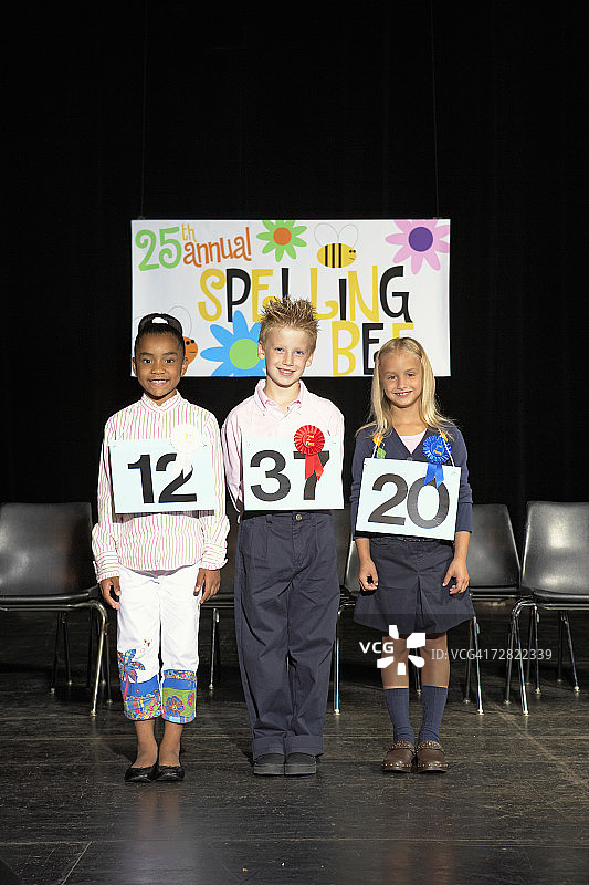 三个孩子（7-9岁）站在拼字比赛的舞台上图片素材