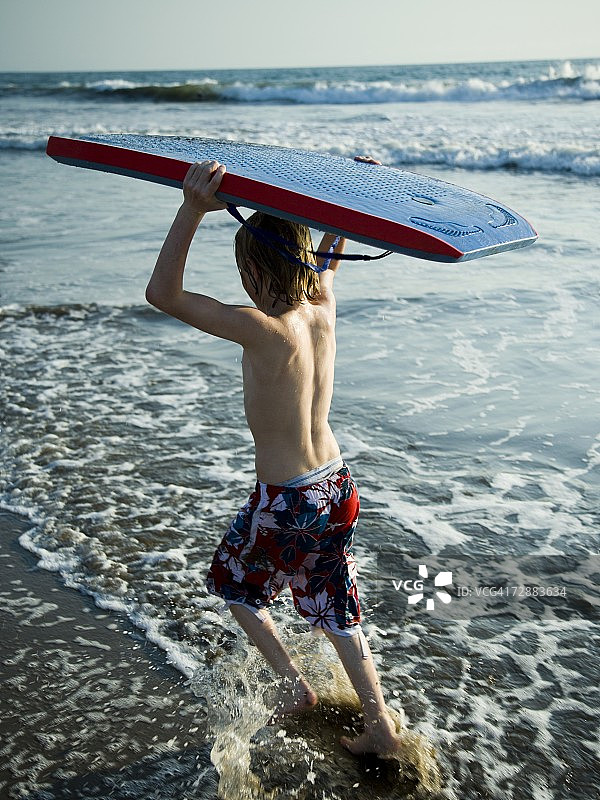 男孩在海滩上带着趴板奔跑图片素材