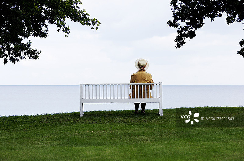 坐在长椅上眺望大海的老年妇女（后视图）图片素材