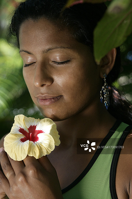 女人闭着眼睛在户外闻着黄色的芙蓉花，特写图片素材