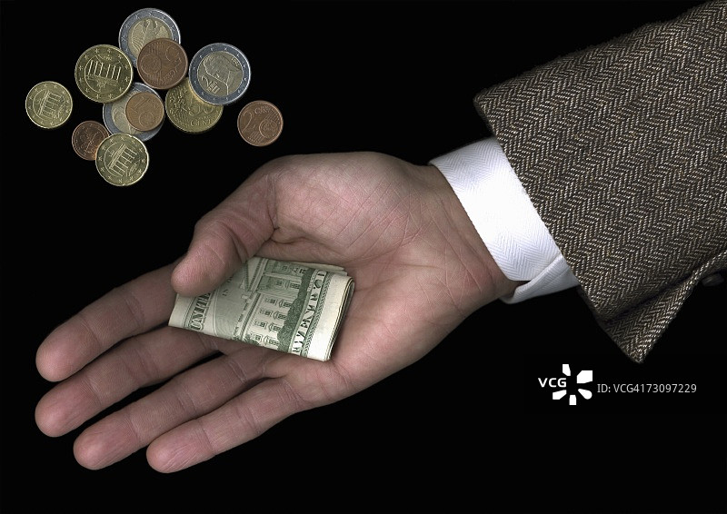男人手持美元站在欧元硬币堆旁图片素材