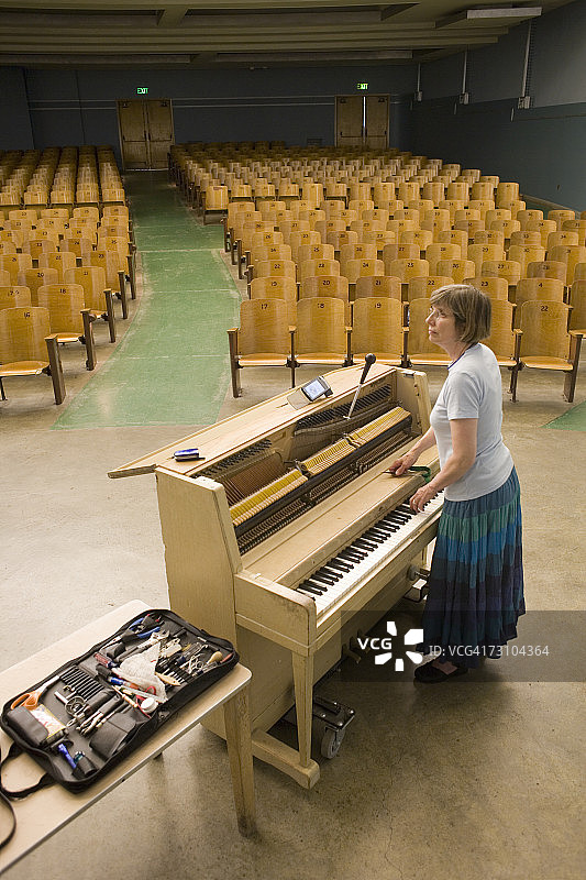 站在钢琴旁讲台上的中年妇女钢琴调音师，高角度视角图片素材
