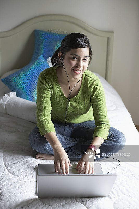 坐在床上使用笔记本电脑的少女图片素材