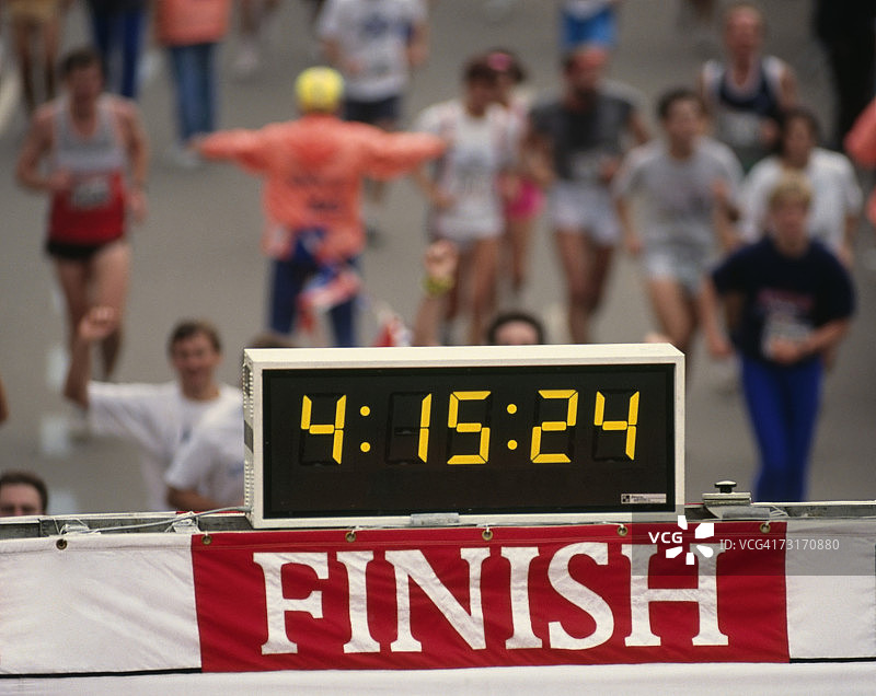 马拉松比赛终点线的计时钟和冲过终点线的跑步者图片素材
