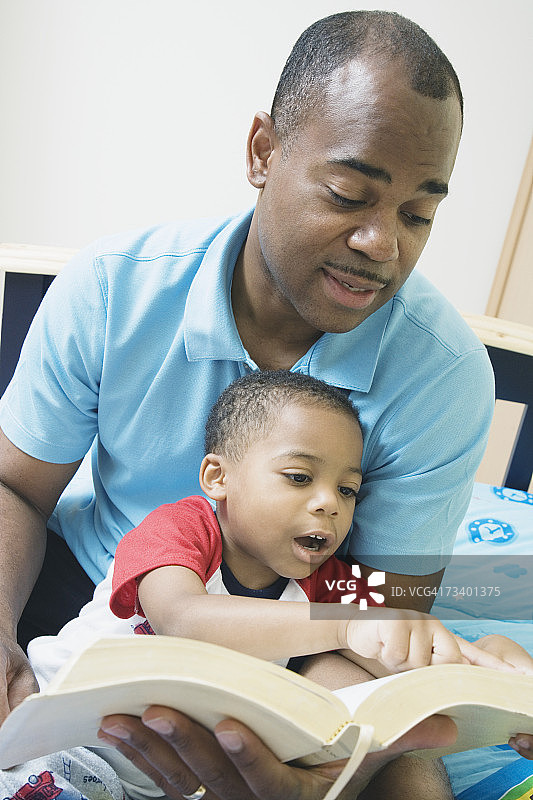父子（4-5岁）在床上阅读圣经，微笑特写图片素材