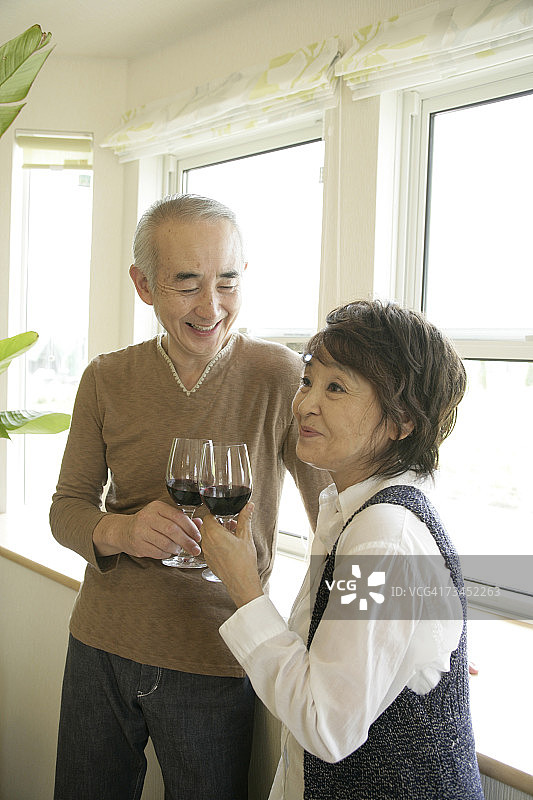 年长夫妇站在窗边，手持红酒杯图片素材