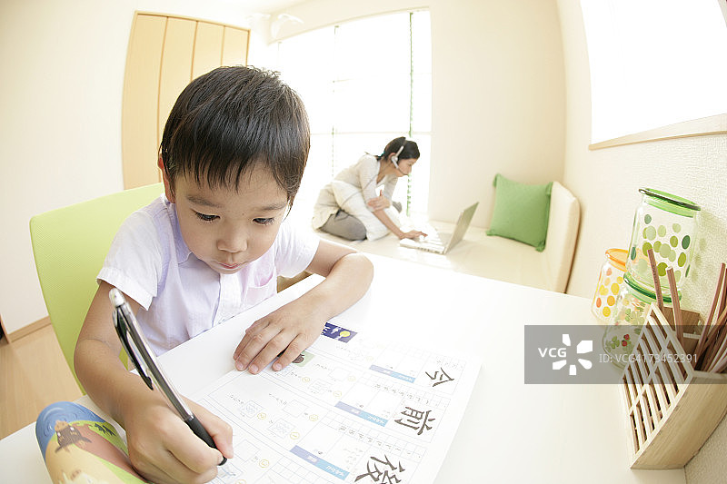 男孩在纸上写字，妹妹在背景中使用笔记本电脑特写图片素材