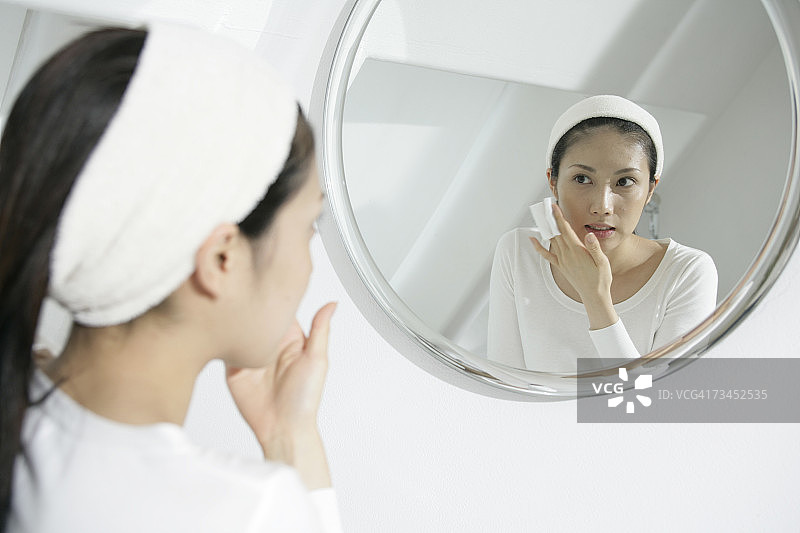在镜子前用纸巾擦脸的年轻女人特写图片素材