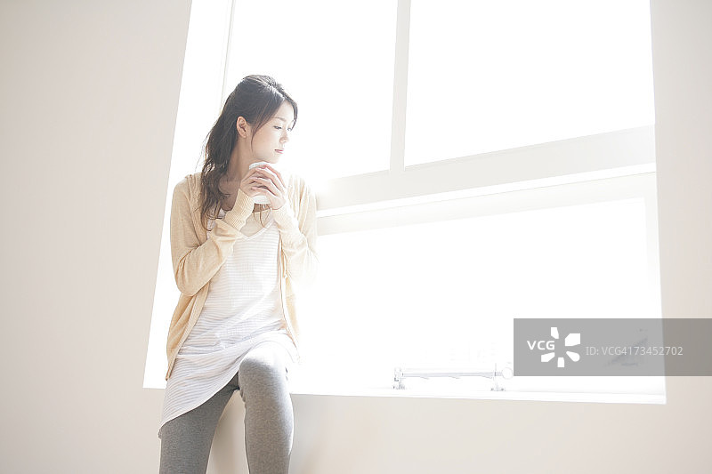 年轻女人在窗台上拿着马克杯放松图片素材
