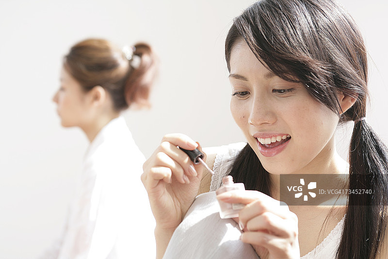 年轻女人手持指甲油，另一年轻女人在背景中特写图片素材