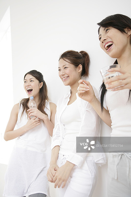 三个年轻女子靠在墙上微笑的仰视角度图片素材