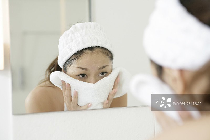 年轻女人在镜子里用毛巾擦脸的倒影图片素材