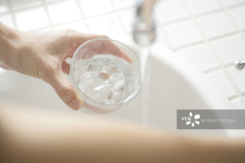 女人的手从水龙头往玻璃杯里倒水的俯视角度照片图片素材