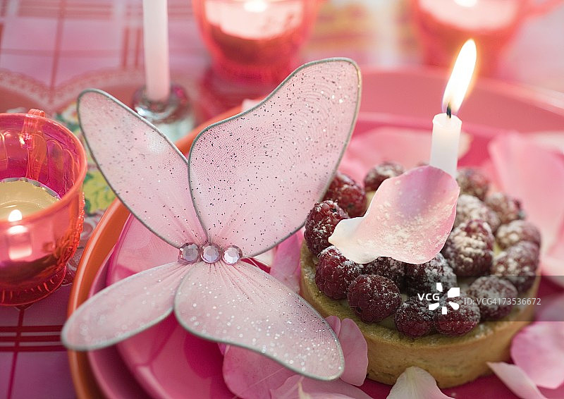 覆盆子小馅饼，盘子上装饰着蜡烛、蝴蝶和玫瑰花瓣图片素材