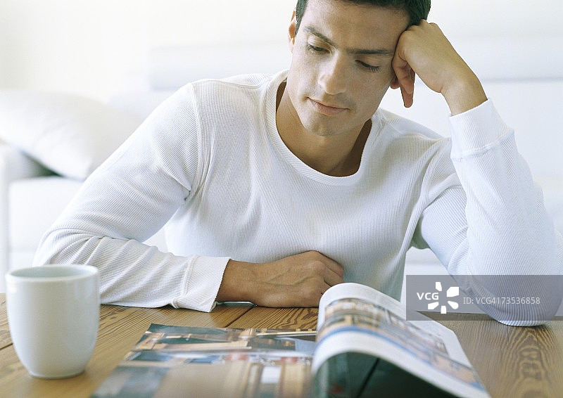 男子坐在桌旁看书，旁边放着咖啡杯图片素材