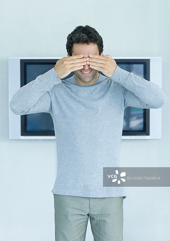 站在墙上宽屏电视前，用手遮住眼睛的男人图片素材