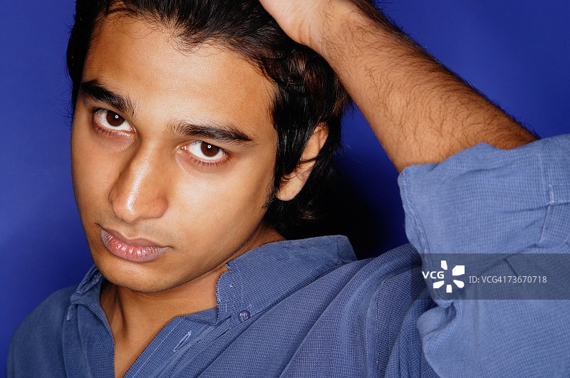 穿蓝色衬衫的男人，蓝色背景，手放在头上图片素材