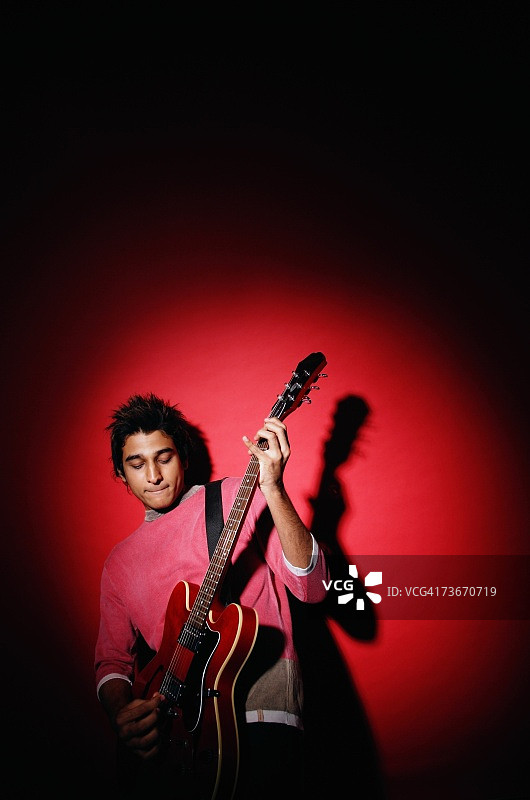 年轻男人弹吉他，背景为红色图片素材