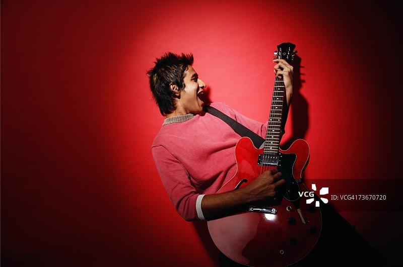 年轻男人弹吉他，背景为红色图片素材