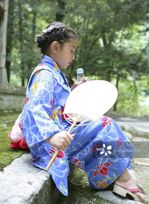 亚洲女孩身穿日式浴衣，坐在岩石上图片素材