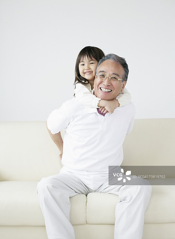 女孩在沙发上搂着祖父的脖子微笑图片素材