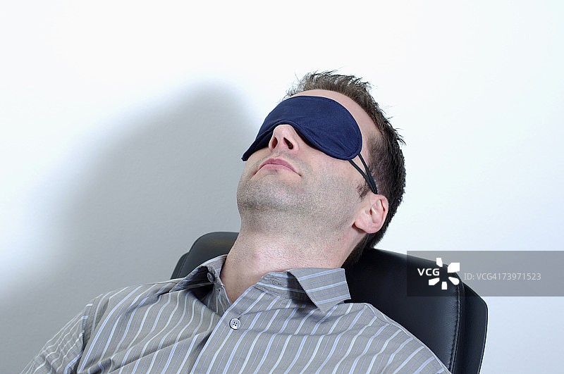 戴着睡眠眼罩向后靠在椅子上的办公室职员图片素材
