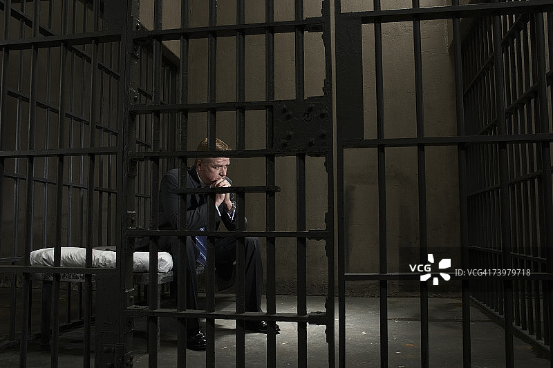 年长的商人坐在监狱牢房的床上图片素材
