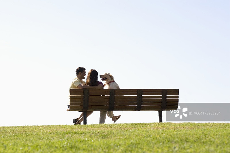情侣和他们的狗坐在公园的长椅上图片素材