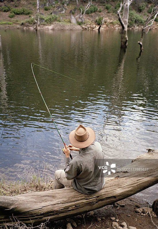 男人在河岸的木头上钓鱼图片素材