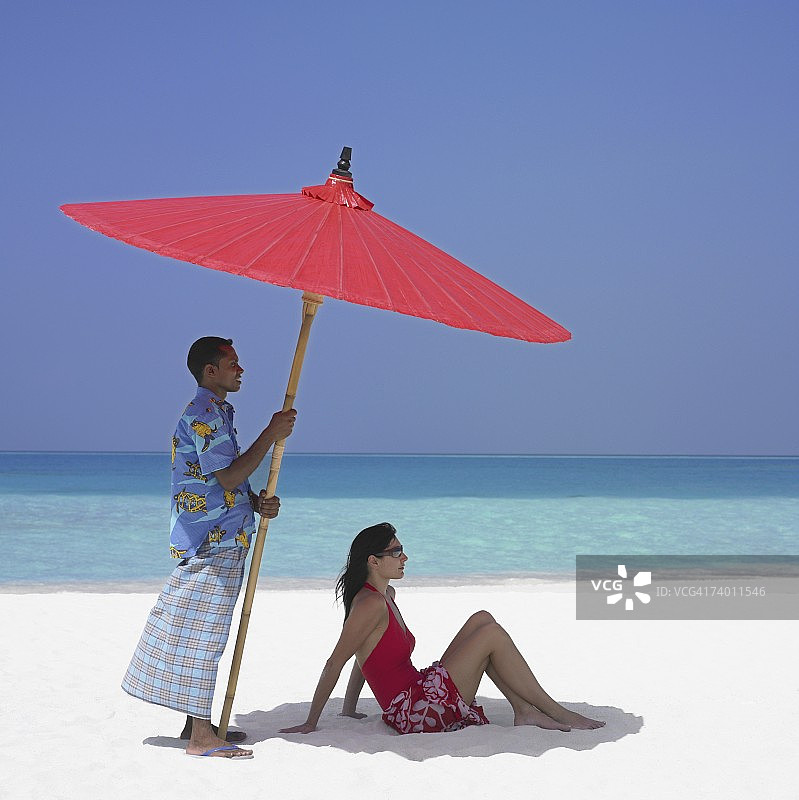 马尔代夫男人为女人撑沙滩伞图片素材