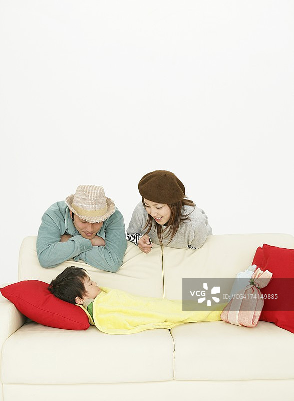 日本夫妇看着在沙发上睡觉的男孩图片素材