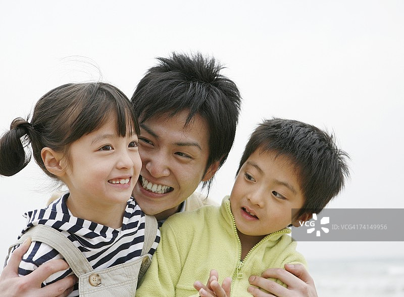 日本男人在沙滩上抱着两个孩子图片素材