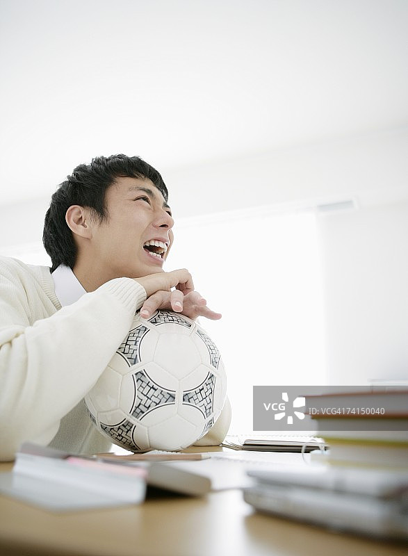 手托足球思考的日本青年男子图片素材