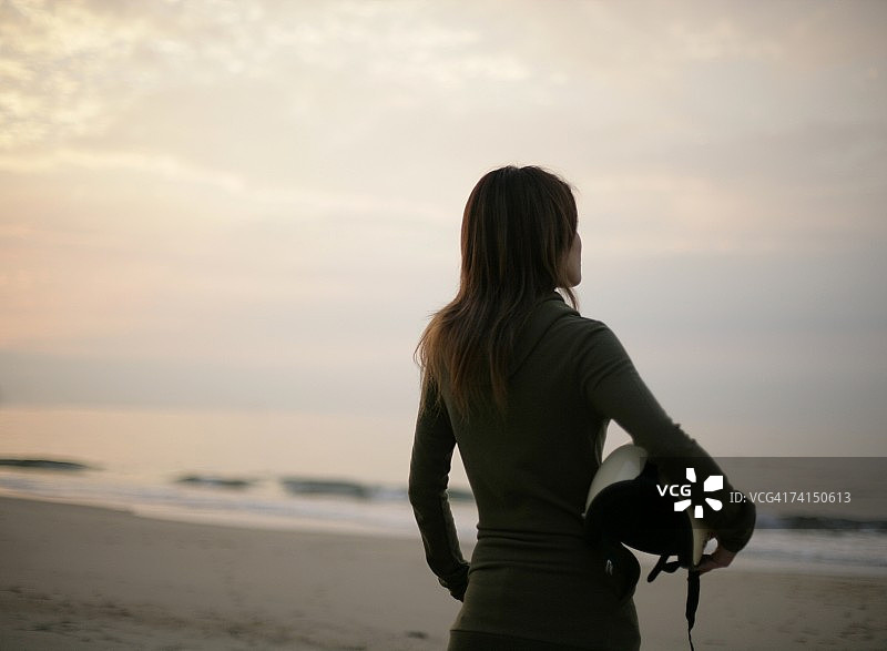 在海滩上拿着头盔看日落的日本女人图片素材