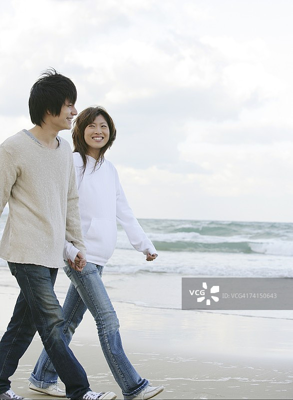 在沙滩上牵手行走的日本年轻夫妇图片素材