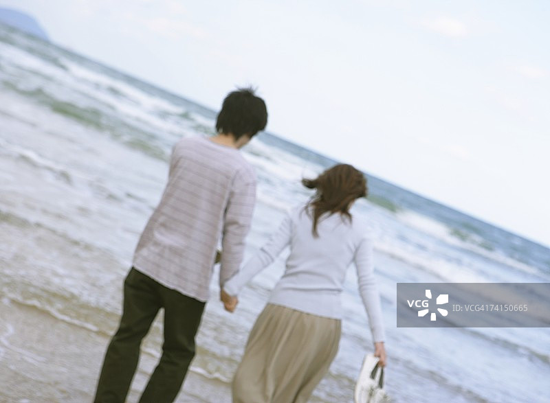 在沙滩上牵手行走的日本年轻夫妇图片素材