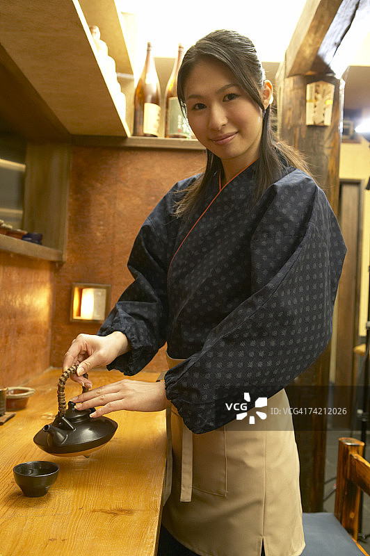 年轻女人往杯子里倒茶图片素材