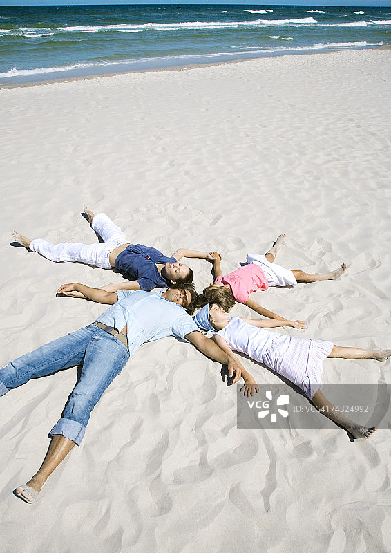 一家人躺在沙滩上，头靠在一起，手脚伸展开来图片素材