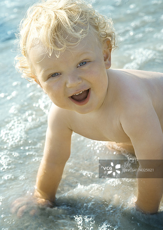 在海浪中玩耍，对着镜头微笑的幼儿肖像图片素材