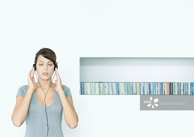 年轻女人闭着眼睛，戴着耳机站在CD架旁听音乐图片素材
