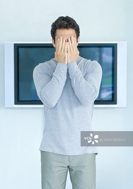 男人站在宽屏电视前，双手捂着脸图片素材