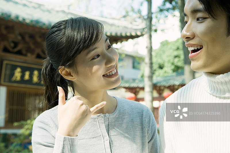 站在男人旁边的女人，做打电话手势，背景是中国传统建筑图片素材