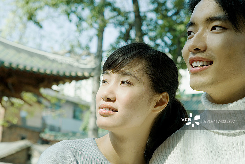 情侣并肩站立，看向镜头外，背景为中国传统建筑图片素材