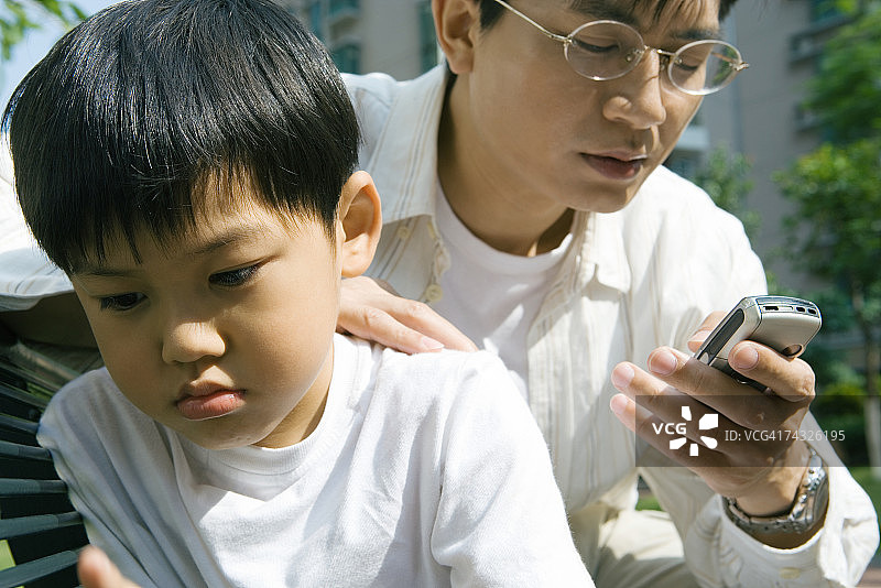 男人看手机，儿子不悦地看向别处图片素材