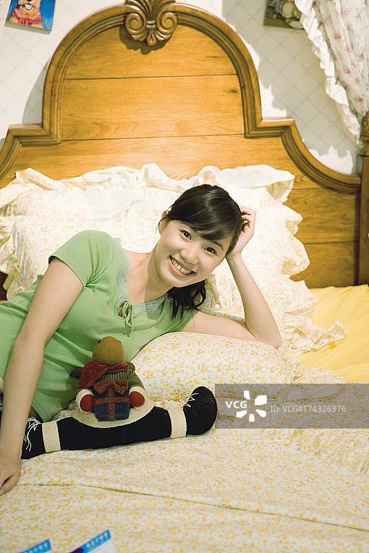 年轻女子斜靠在床上，对着镜头微笑图片素材
