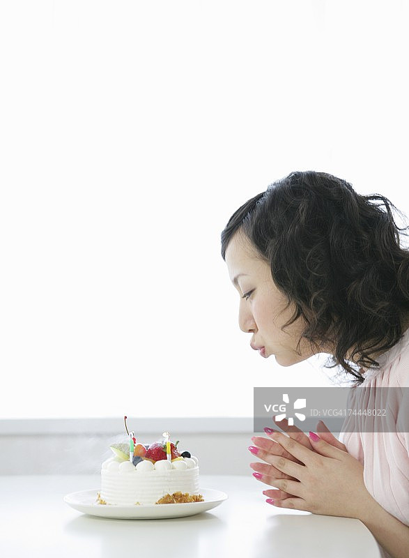 在生日蛋糕上吹灭蜡烛的日本女人图片素材