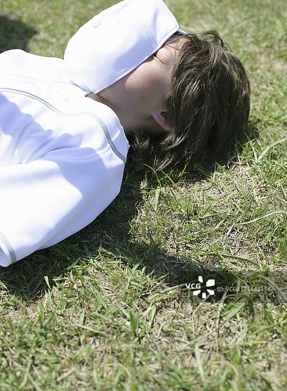 戴棒球帽、穿棒球服的男孩躺在球场上遮住脸图片素材