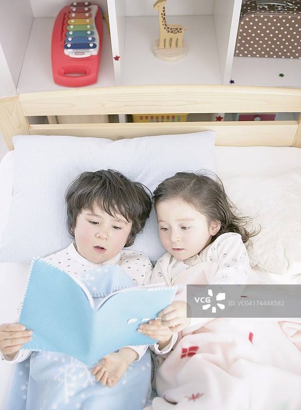加拿大女孩和男孩在床上躺着读书图片素材