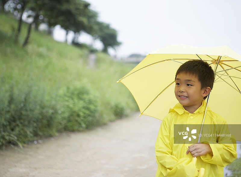 穿着黄色雨衣、撑着伞的日本男孩图片素材