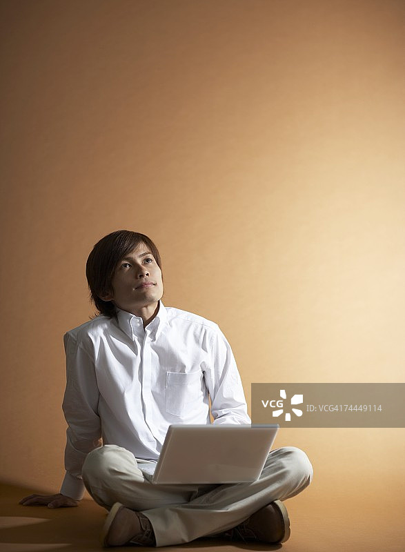日本男人膝盖上放着笔记本电脑，若有所思图片素材